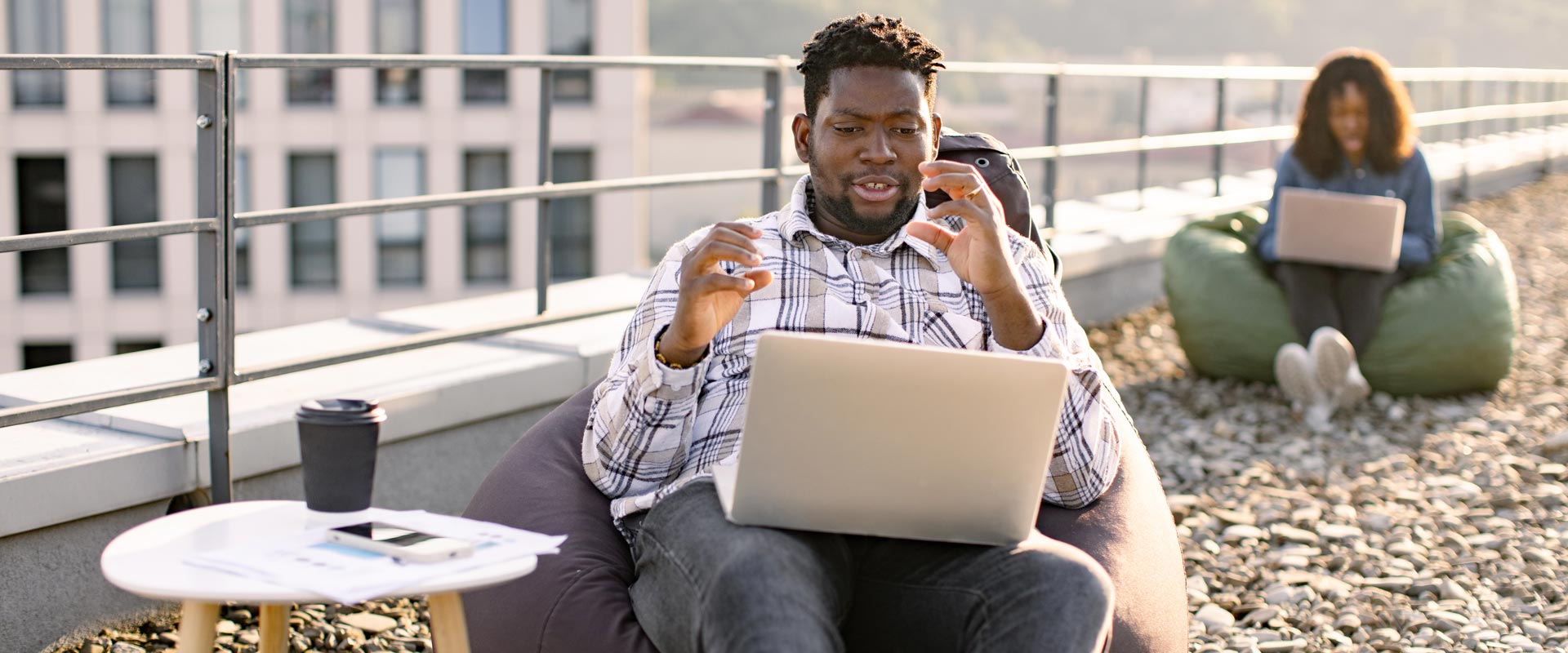 Man on rooftop using a laptop, gesturing while video chatting.